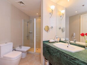 A bathroom with a shower, toilet, bidet, and a sink with a large mirror.