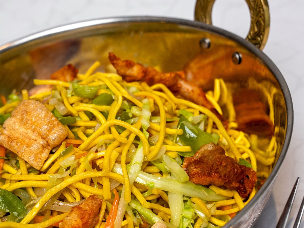 A stainless steel pan filled with stir-fried noodles, vegetables, and pieces of meat.