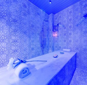 A blue-lit room with a patterned wall, a massage table, and a small shelf with items.
