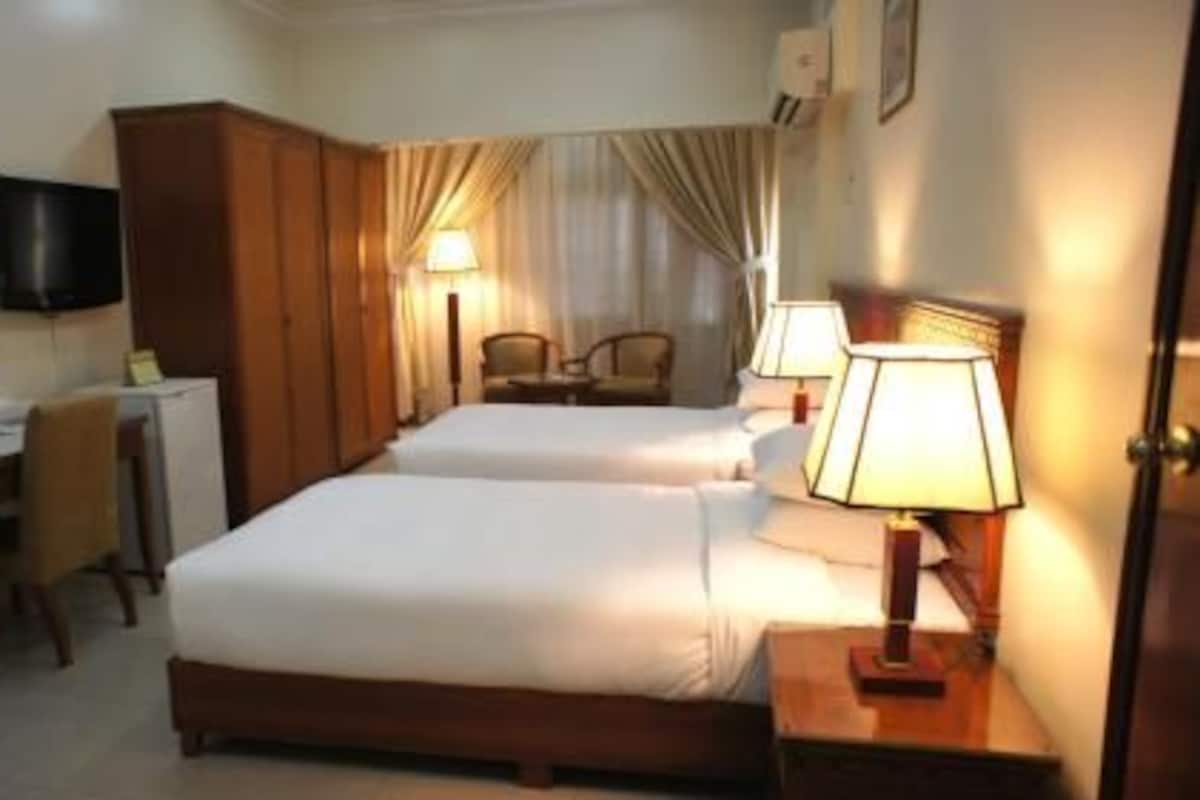 A hotel room with two beds, a desk with a chair, a television, and two bedside lamps.