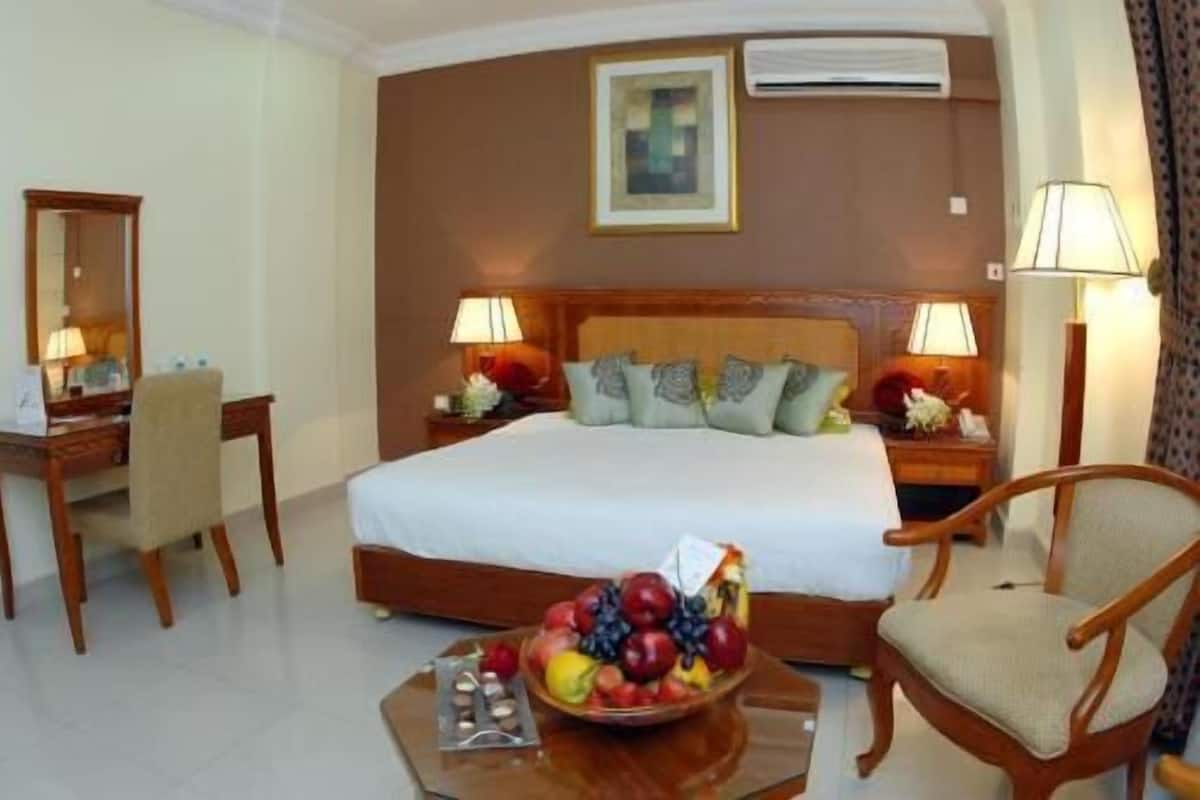 Une chambre d’hôtel comprenant un lit, deux tables de chevet, un bureau, une chaise, un panier de fruits et deux lampes.
