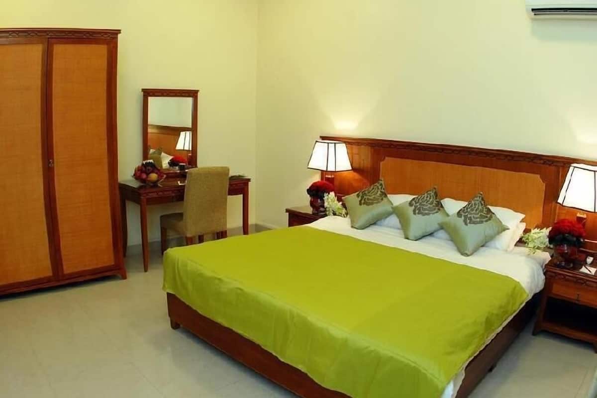 Une chambre d’hôtel comprenant un lit, un bureau, une chaise, une armoire et une table de chevet avec une lampe.