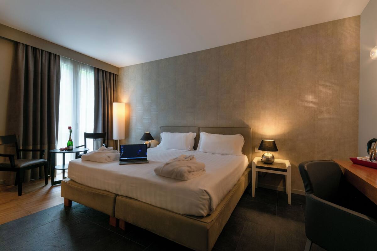 Une chambre d’hôtel avec un grand lit, un bureau, une chaise, un ordinateur portable et une lampe.