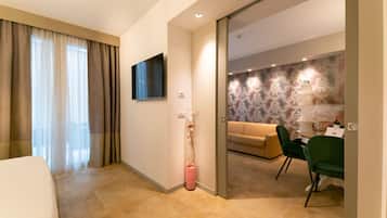 A hotel room with a bed, a TV mounted on the wall, a desk with a chair, and a sofa in the adjacent living area.