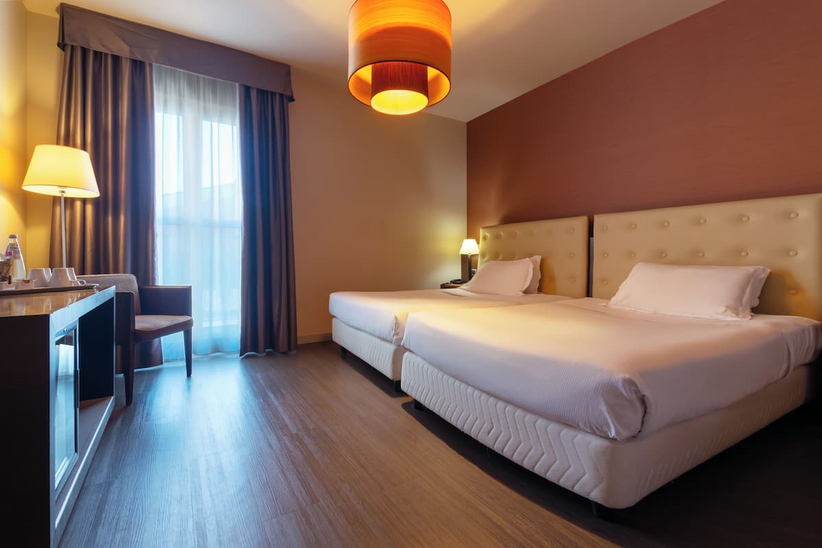 Une chambre d’hôtel avec deux lits, un bureau, une chaise et une grande fenêtre avec des rideaux.