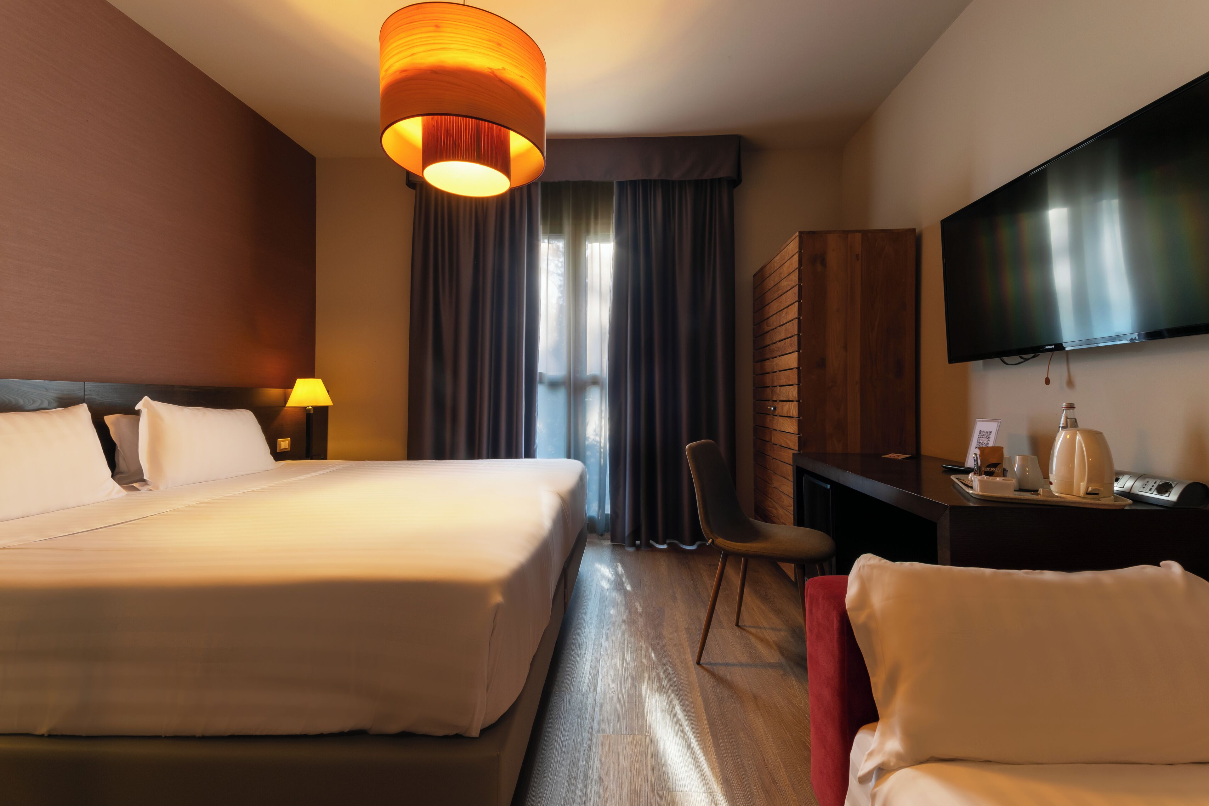 Une chambre d’hôtel avec un grand lit, un bureau avec une chaise, une télévision et une fenêtre avec des rideaux.
