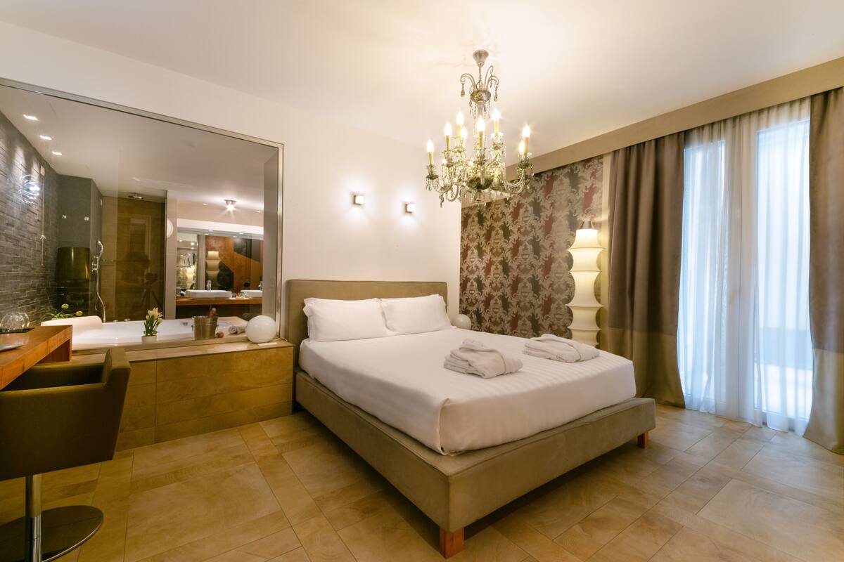 Une chambre d’hôtel moderne dotée d’un grand lit, d’un bureau et d’une salle de bain visible à travers une paroi en verre.