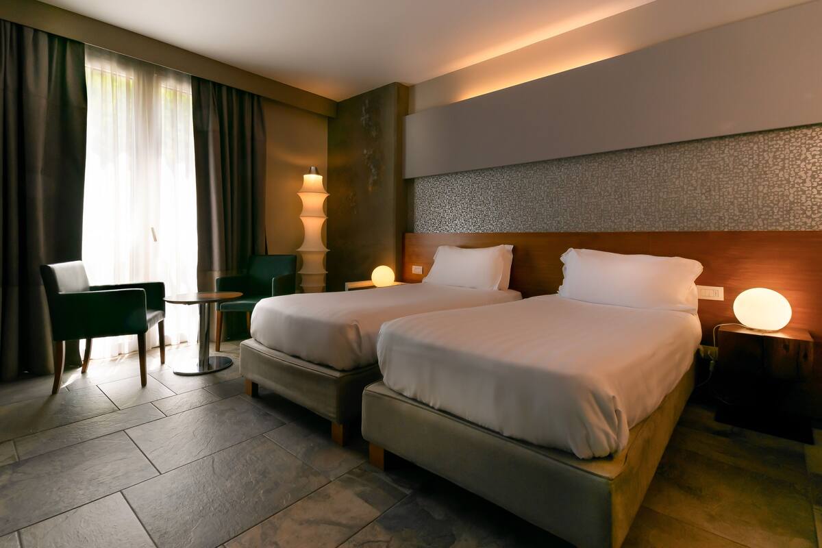 Une chambre d’hôtel avec deux lits, un bureau, une chaise et une lampe.