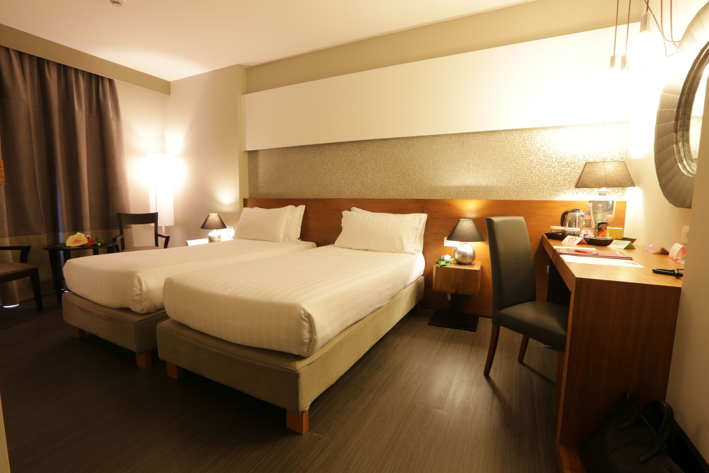 Een hotelkamer met twee bedden, een bureau, een stoel en een tafeltje met een lamp.