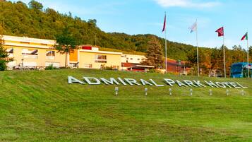 The Admiral Park Hotel sign on a grassy hill with flags, surrounded by buildings and a forested hill in the background.
