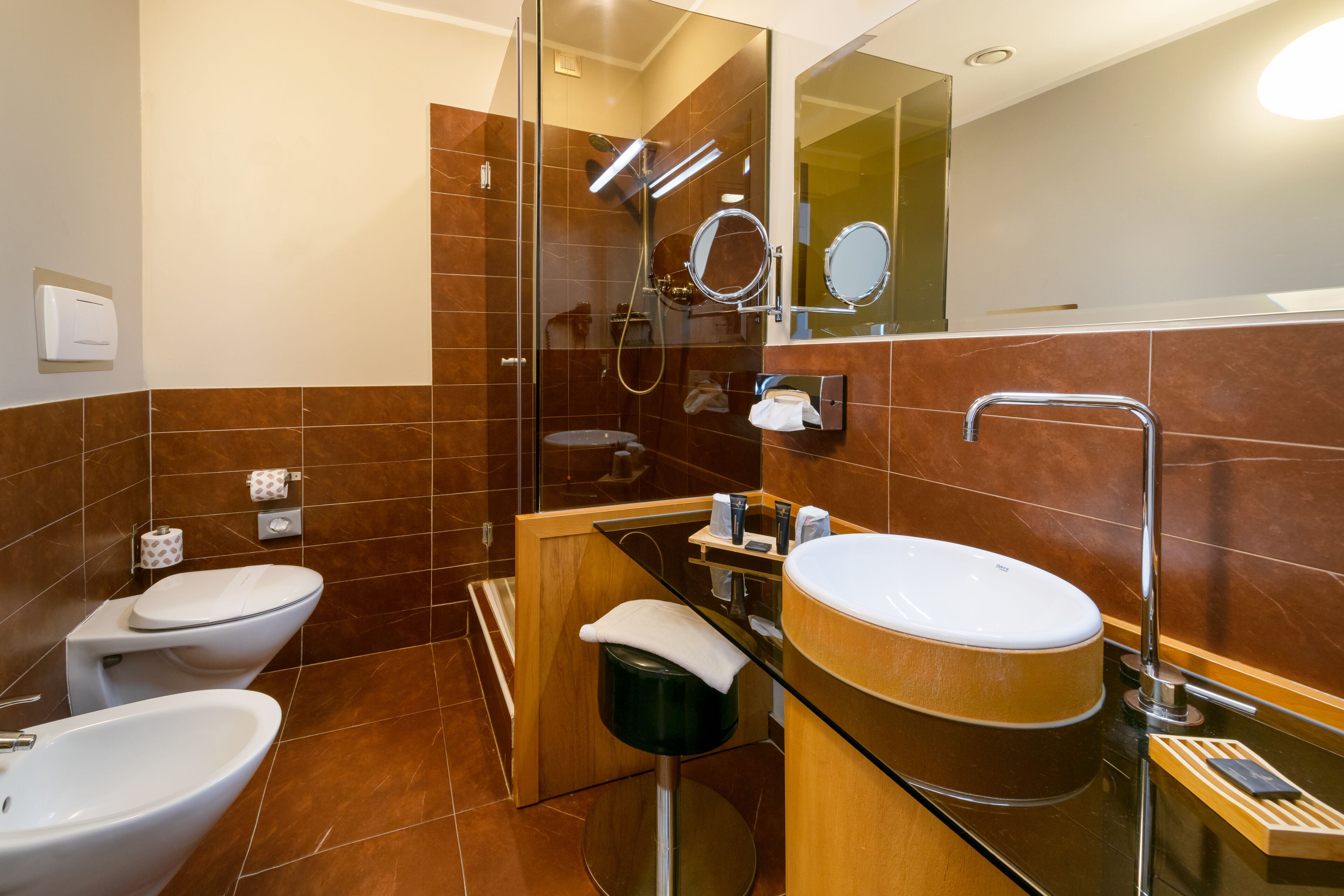 Une salle de bain moderne avec une douche à parois de verre, deux toilettes, un lavabo et un miroir.