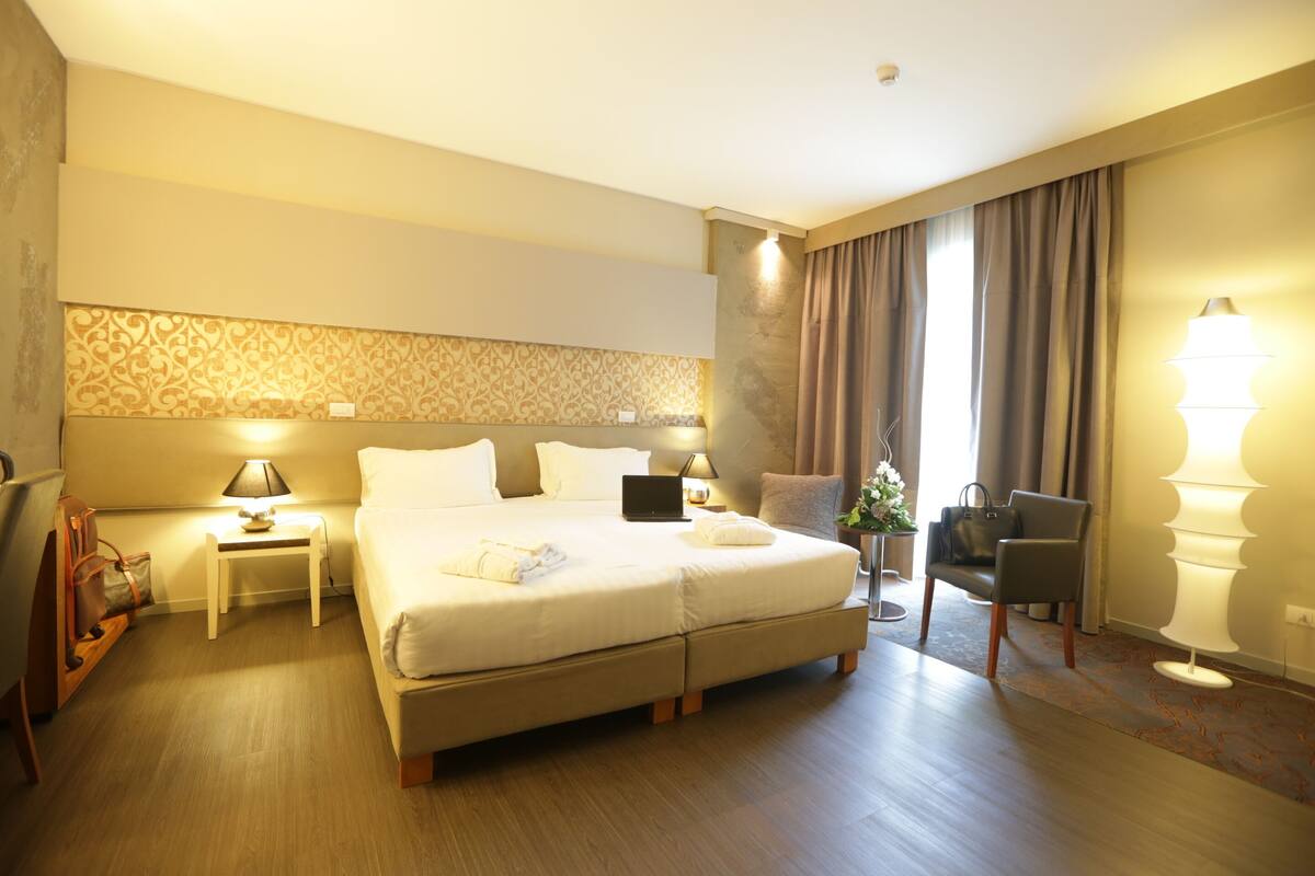 Une chambre d’hôtel avec un grand lit, des tables de chevet avec des lampes, une chaise et un bureau avec un ordinateur portable.