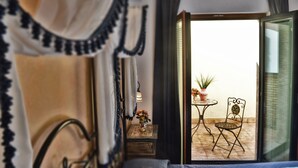 Una habitación con cama, una mesita con planta en maceta y una silla frente a un ventanal que da a un balcón con mesa y sillas.