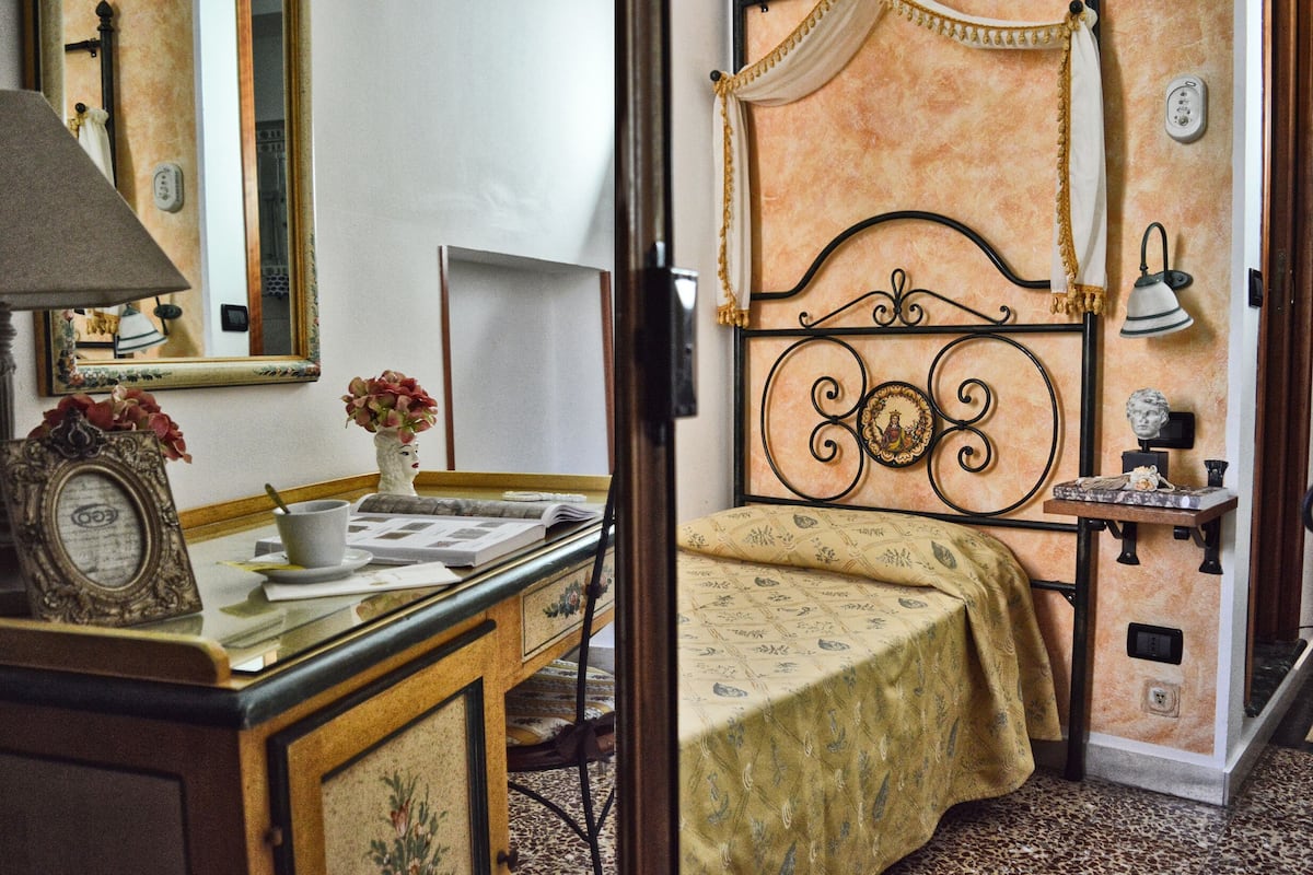 Un dormitorio con cama, mesita de noche, lámpara y espejo.