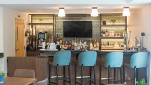 Un espace bar équipé d’un téléviseur à écran plat, de tabourets de bar, d’un comptoir où sont exposées différentes bouteilles et d’une machine à café.