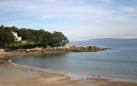 A coastal scene with a sandy beach, rocky outcrops, and a lighthouse in the distance.