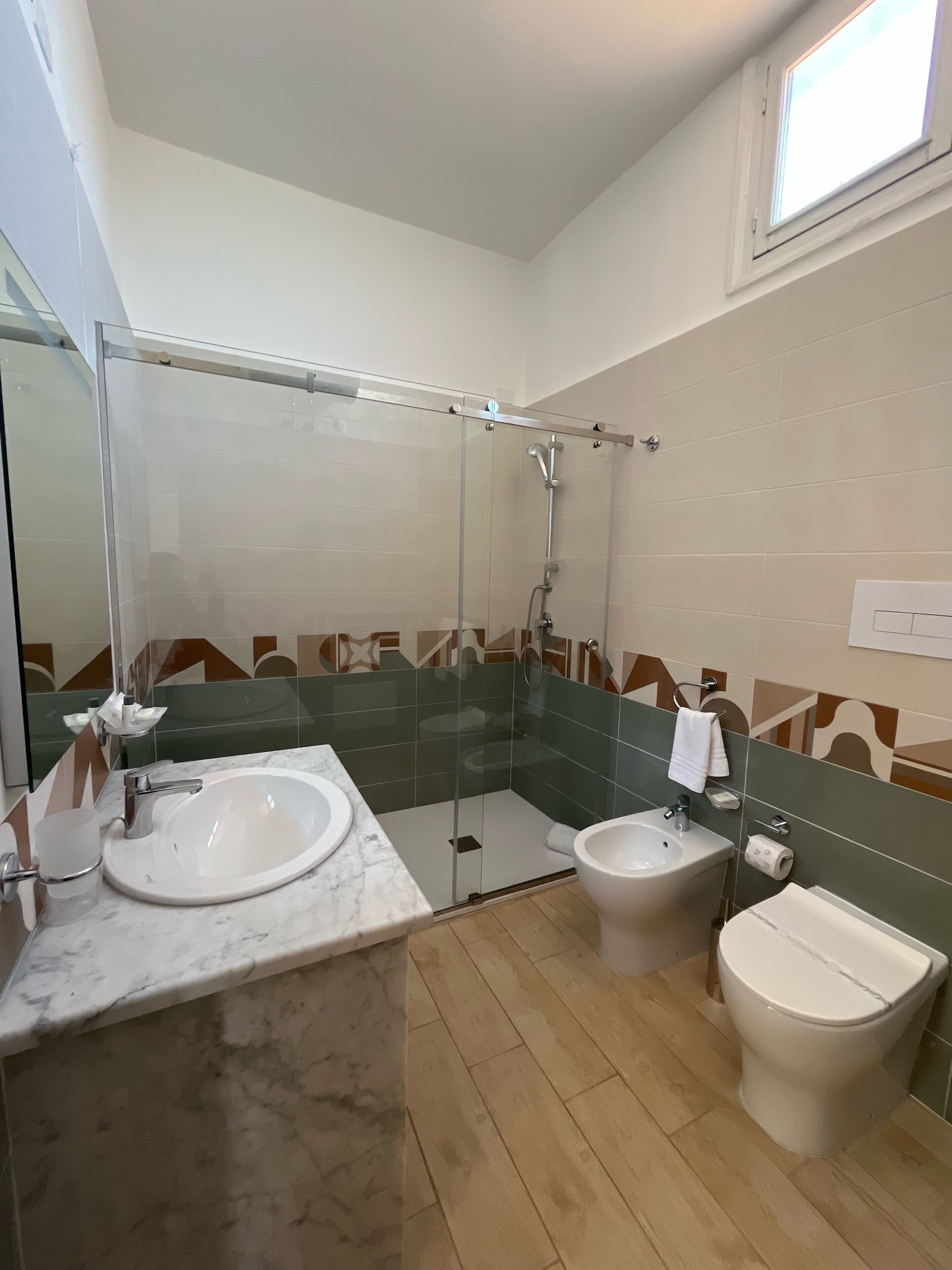 Ein modernes Badezimmer mit einer Duschkabine, zwei Waschbecken, einer Toilette und einem Spiegel.