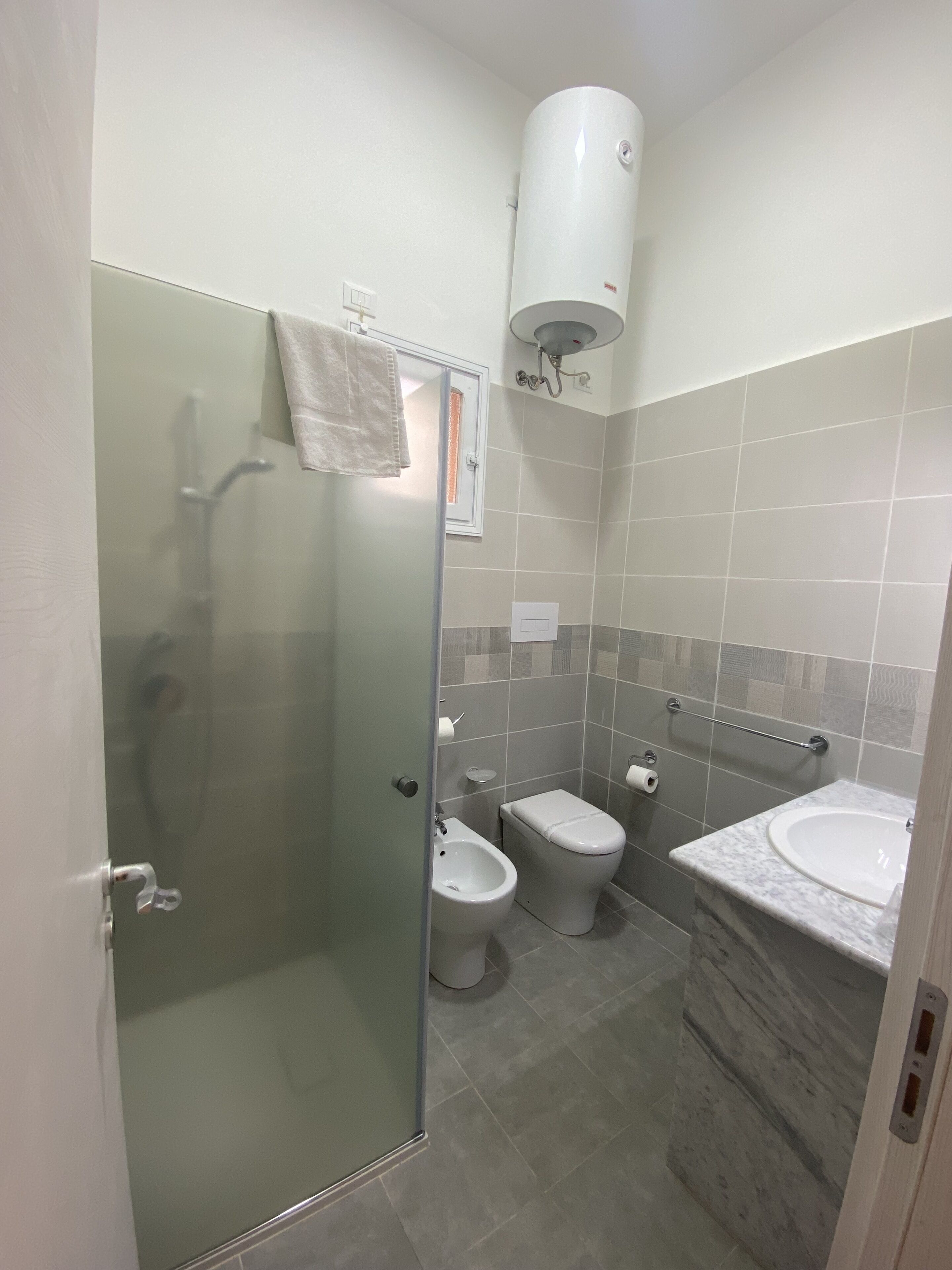 A bathroom with a glass-enclosed shower, a toilet, and a sink with a marble countertop.