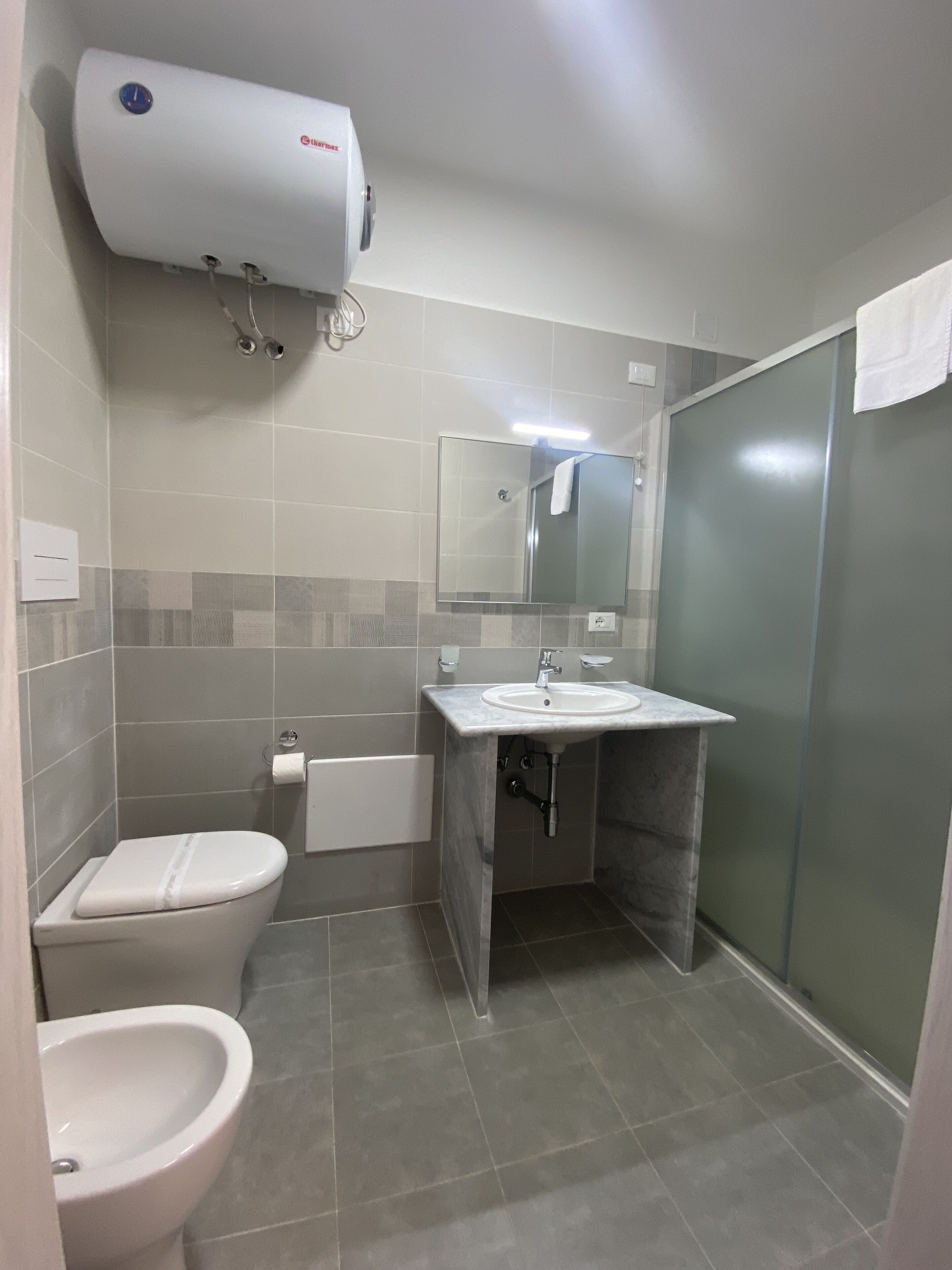 Een badkamer met toilet, bidet, wastafel en spiegel.