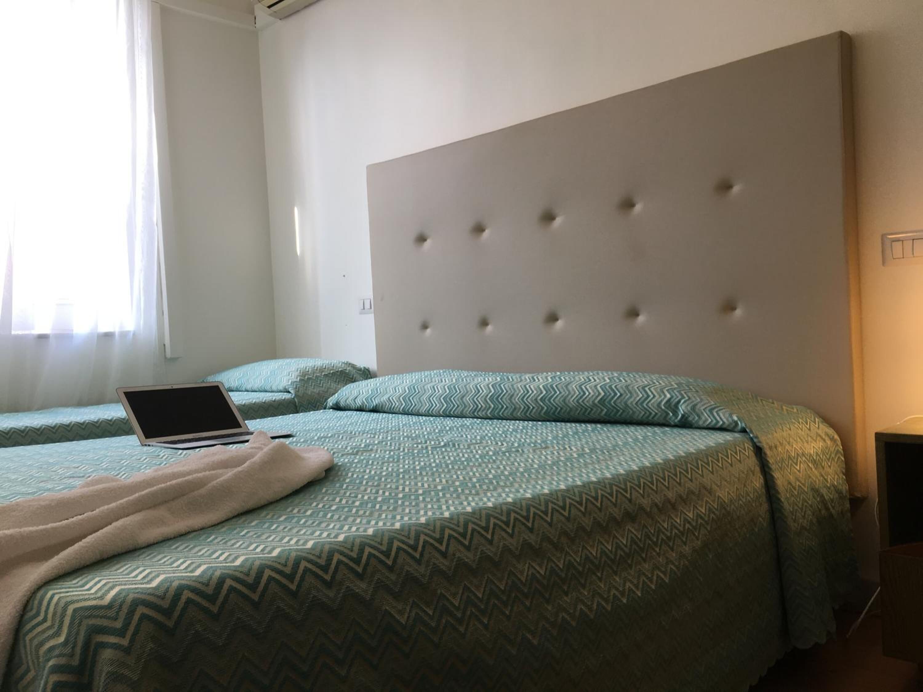 A bedroom with two beds, a laptop on the left bed, and a tufted headboard.
