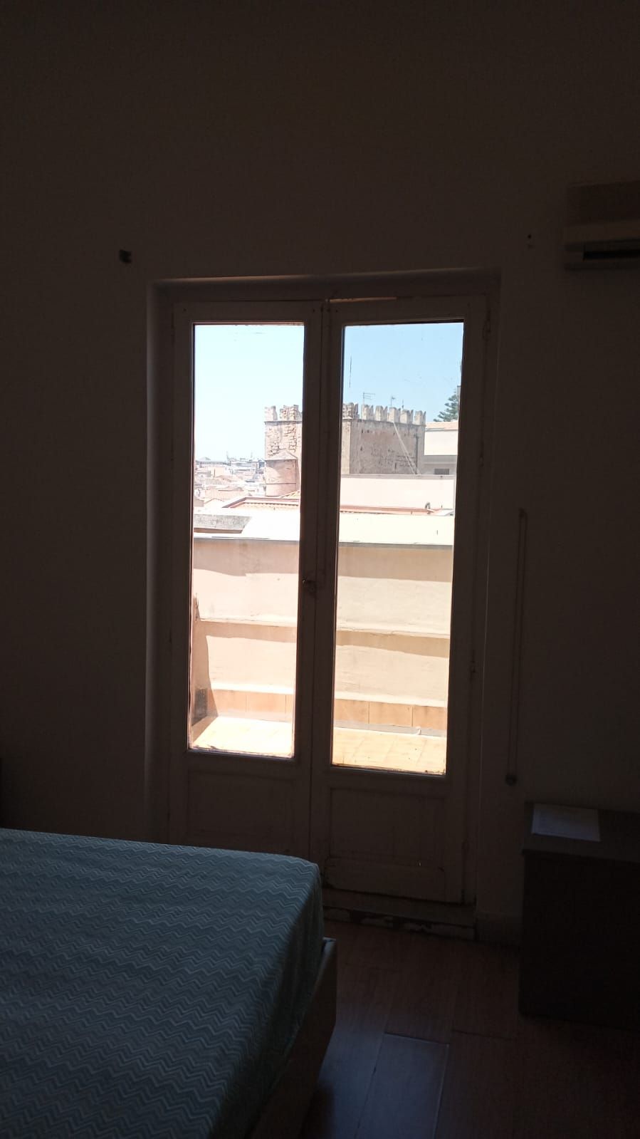 A room with a bed, a door leading to an outdoor terrace, and a trash bin.