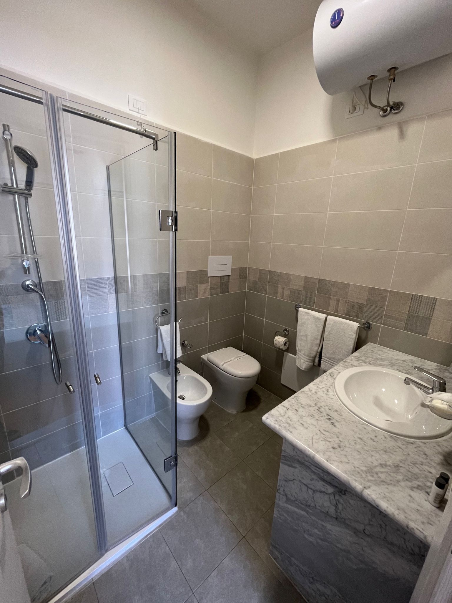 Ein modernes Badezimmer mit einer Duschkabine aus Glas, einem Bidet, einer Toilette und einem мраморным Waschbecken.