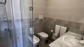 Ein modernes Badezimmer mit einer Duschkabine aus Glas, einem Bidet, einer Toilette und einem мраморным Waschbecken.