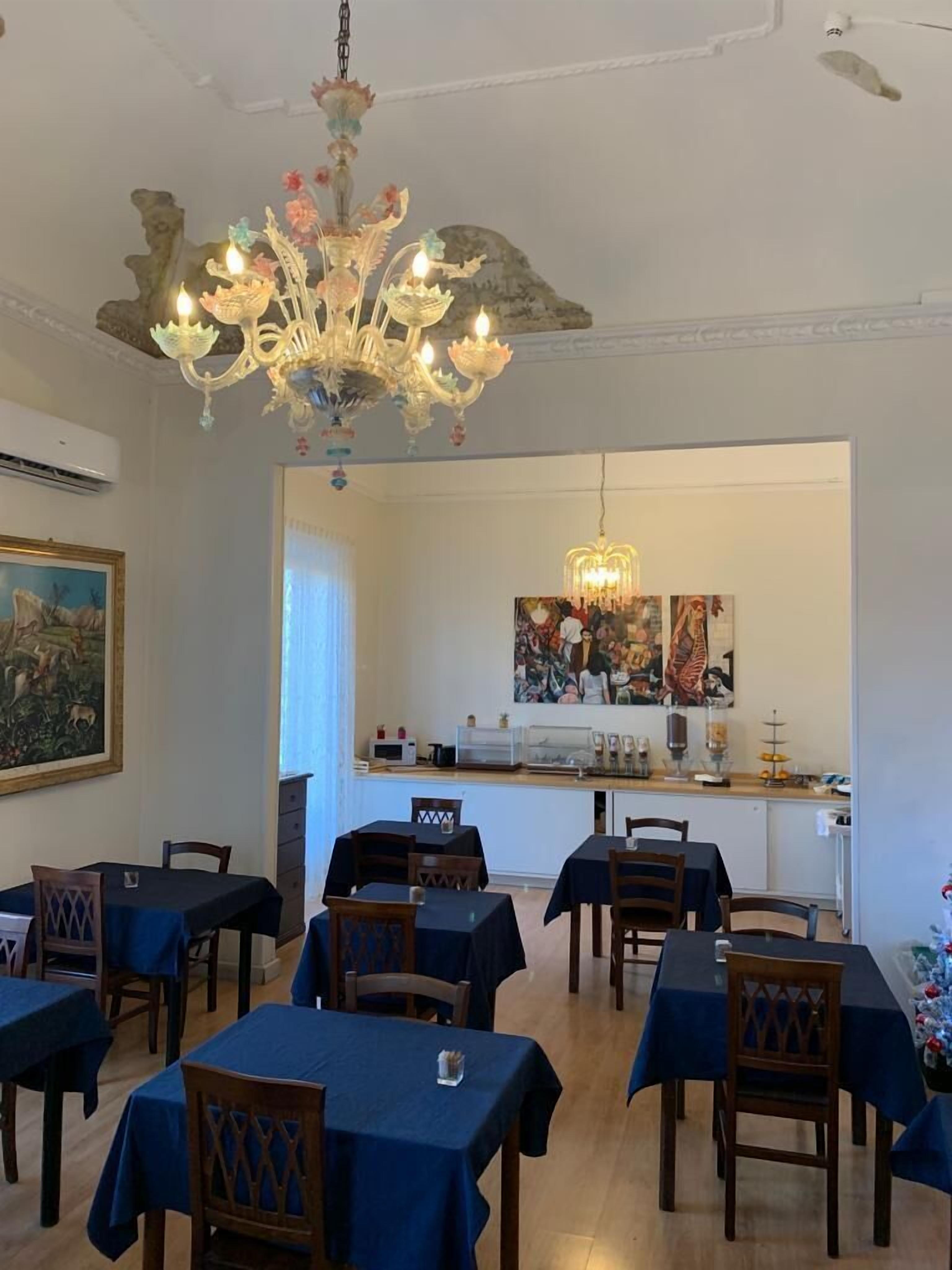 A dining area with tables covered in blue tablecloths, a chandelier, and artwork on the walls.