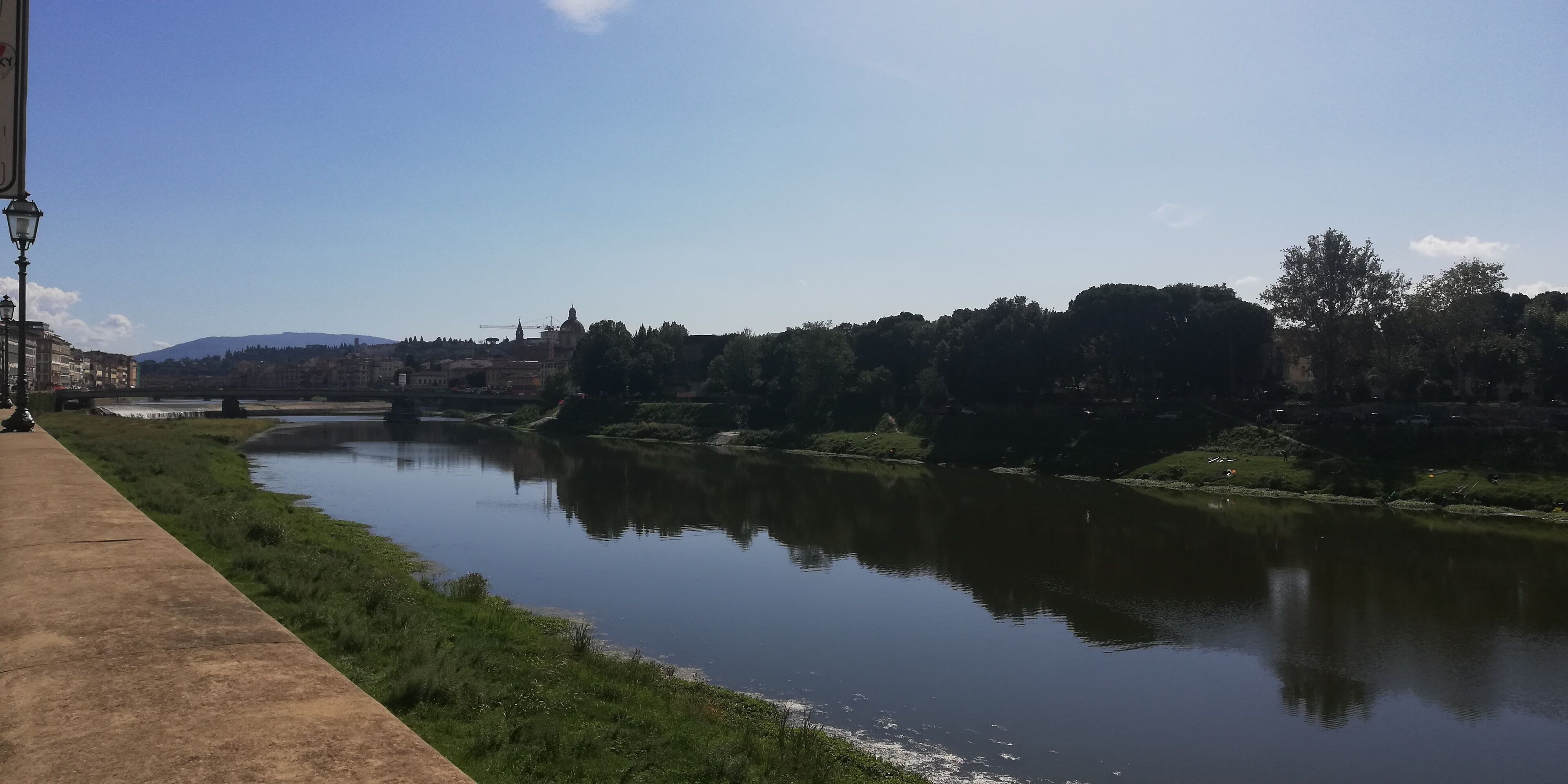 Un río con una pasarela de hormigón a un lado y un puente a lo lejos.