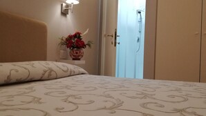 A bedroom with a bed, a wall-mounted light, a vase with flowers, and a door leading to a bathroom. - La Residenza Il Maggio B&B (Florence)
