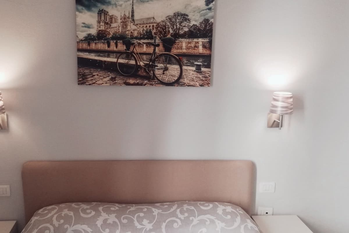Ein Schlafzimmer mit einem Bett, einem Wandbild einer Brücke und Kathedrale sowie zwei Wandleuchten.