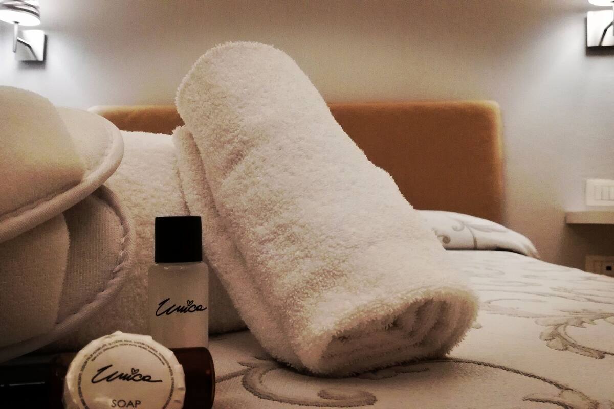 Ein Hotelzimmer mit einem Bett, zwei weißen Handtüchern und einer Flasche Unico-Seife.
