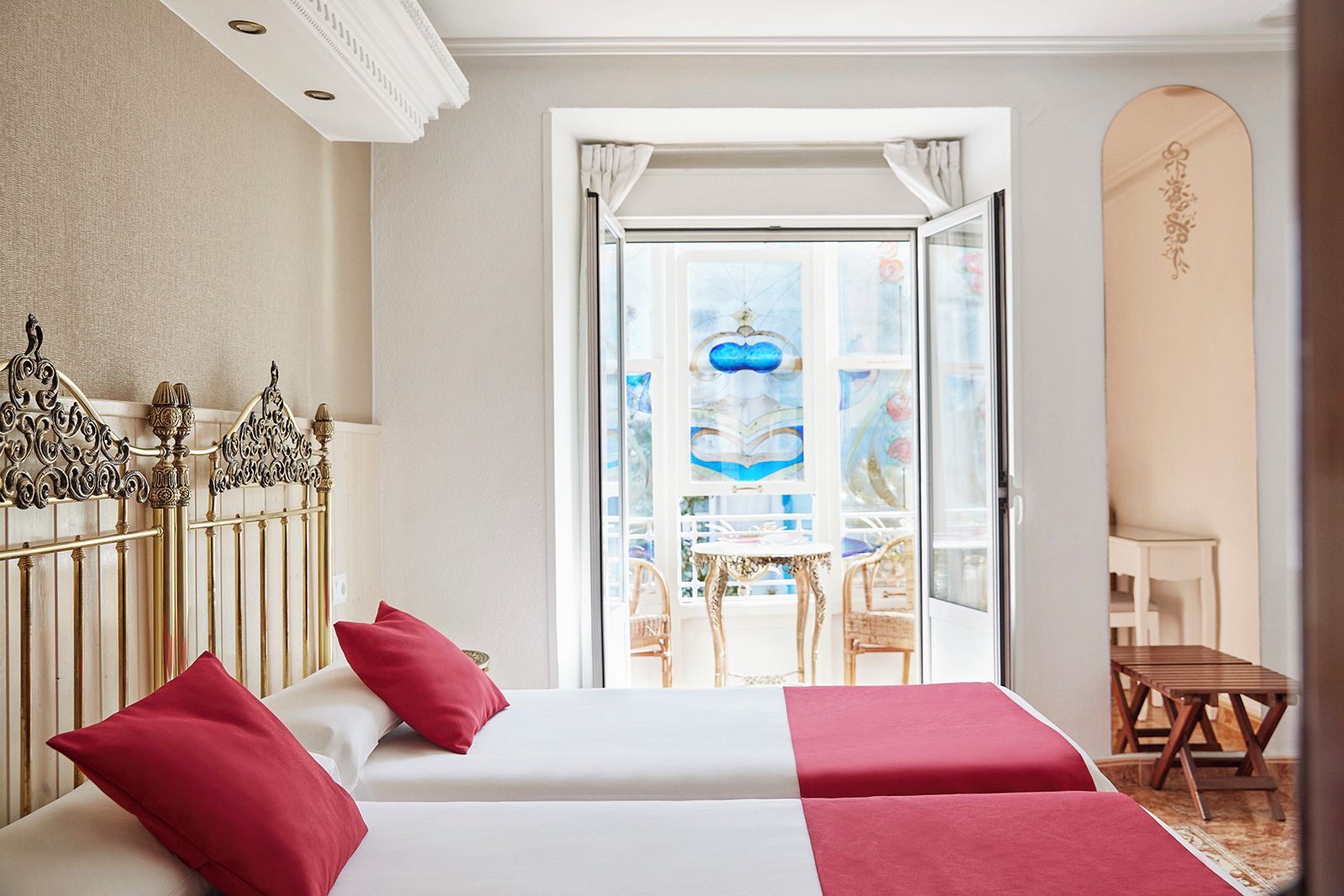 Een hotelkamer met twee bedden, een balkon met uitzicht en een decoratief metalen hoofdbord.