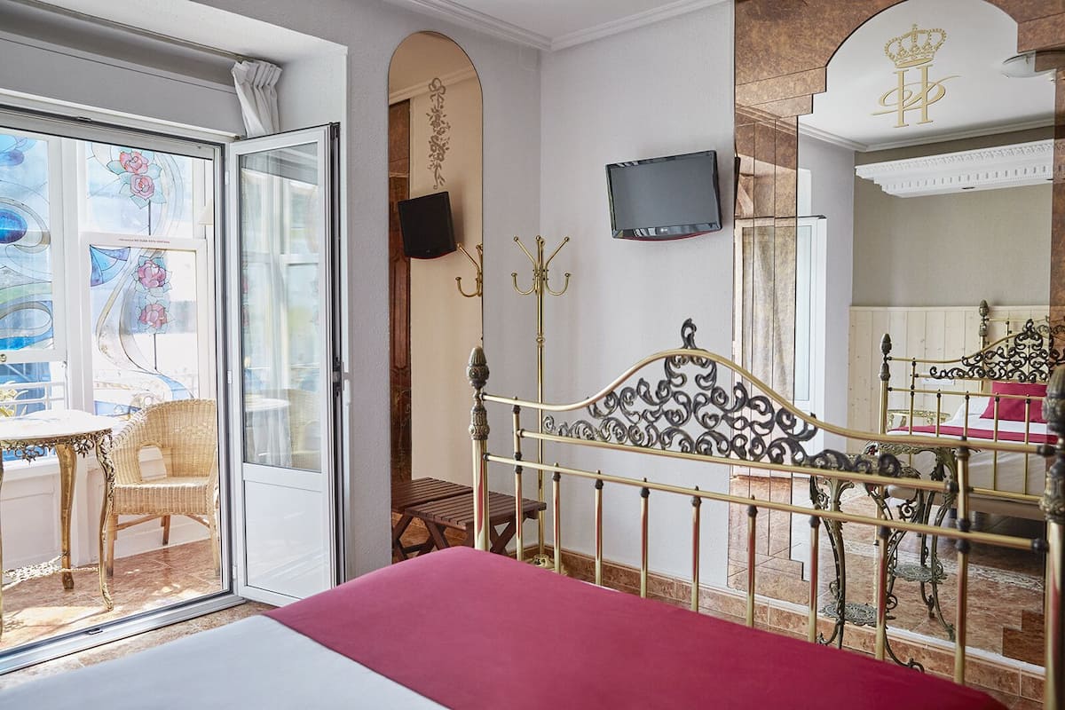 A bedroom with a bed, a television, a balcony with a chair, and a decorative mirror.