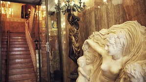 Una escalera de mármol con un letrero que dice 'HOTEL', una estatua de una mujer sosteniendo a un niño y un candelabro.
