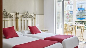 Habitación de hotel con dos camas, un balcón y vistas a un edificio con cúpula azul.