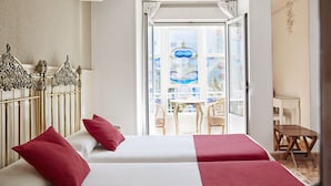 Habitación de hotel con dos camas, un balcón y vistas, y un cabecero decorativo de metal.
