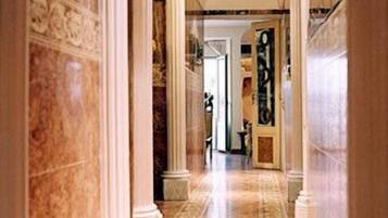 A marble hallway with columns, leading to a room with a large painting.