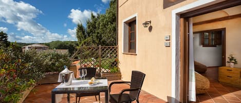 Un patio al aire libre con una mesa preparada para dos, una silla de mimbre y un armario de madera.