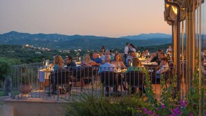 Un espace de restauration en plein air, avec des tables et des chaises, entouré d’une clôture métallique, et offrant une vue sur un paysage montagneux.