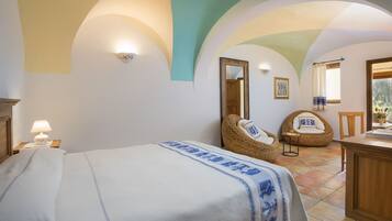A bedroom with a bed, a chair, a table, and a mirror.