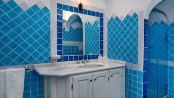 Ein Badezimmer mit einem weißen Waschbecken, zwei Spiegeln und blautonierten Fliesen.