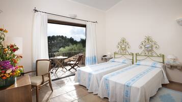 Una habitación con dos camas, un balcón con mesa y sillas, y un florero.