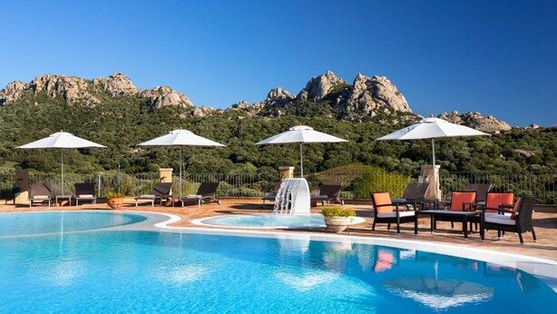 Une piscine entourée de montagnes rocheuses, avec des chaises longues et des parasols.