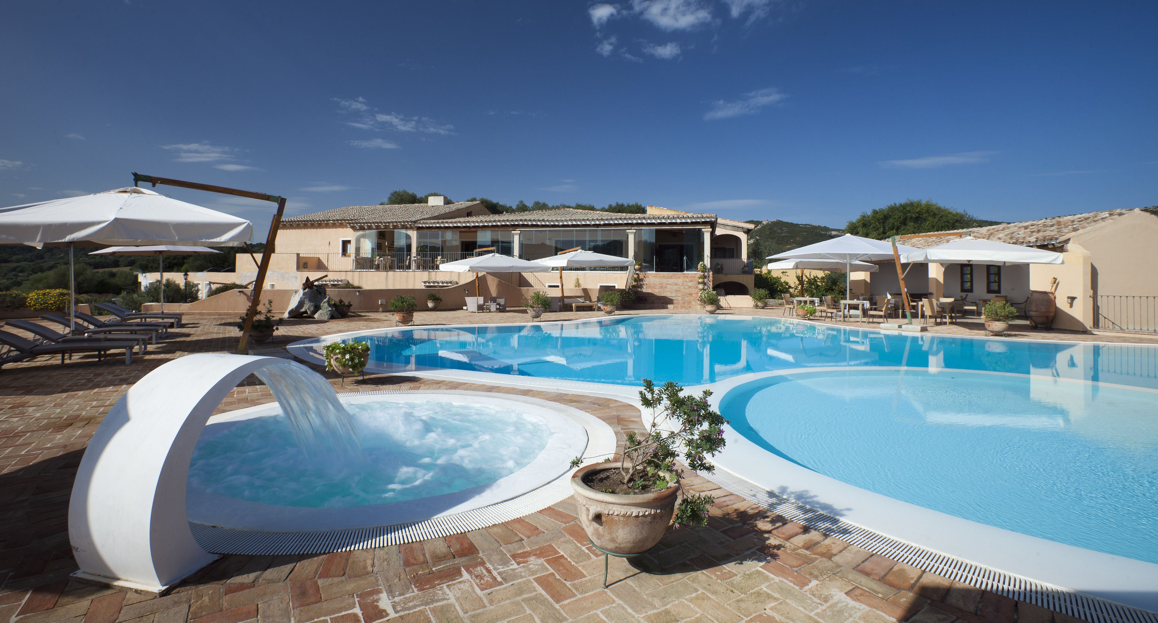 Una piscina amb un banyera d'hidromassatge, gandules i ombrelles.