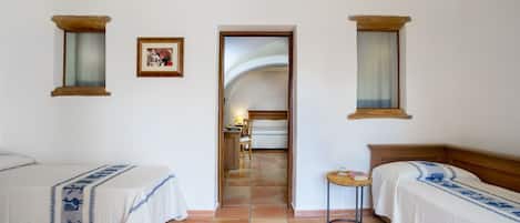Una habitación de hotel con dos camas, una mesita pequeña y una puerta que da a un pasillo.