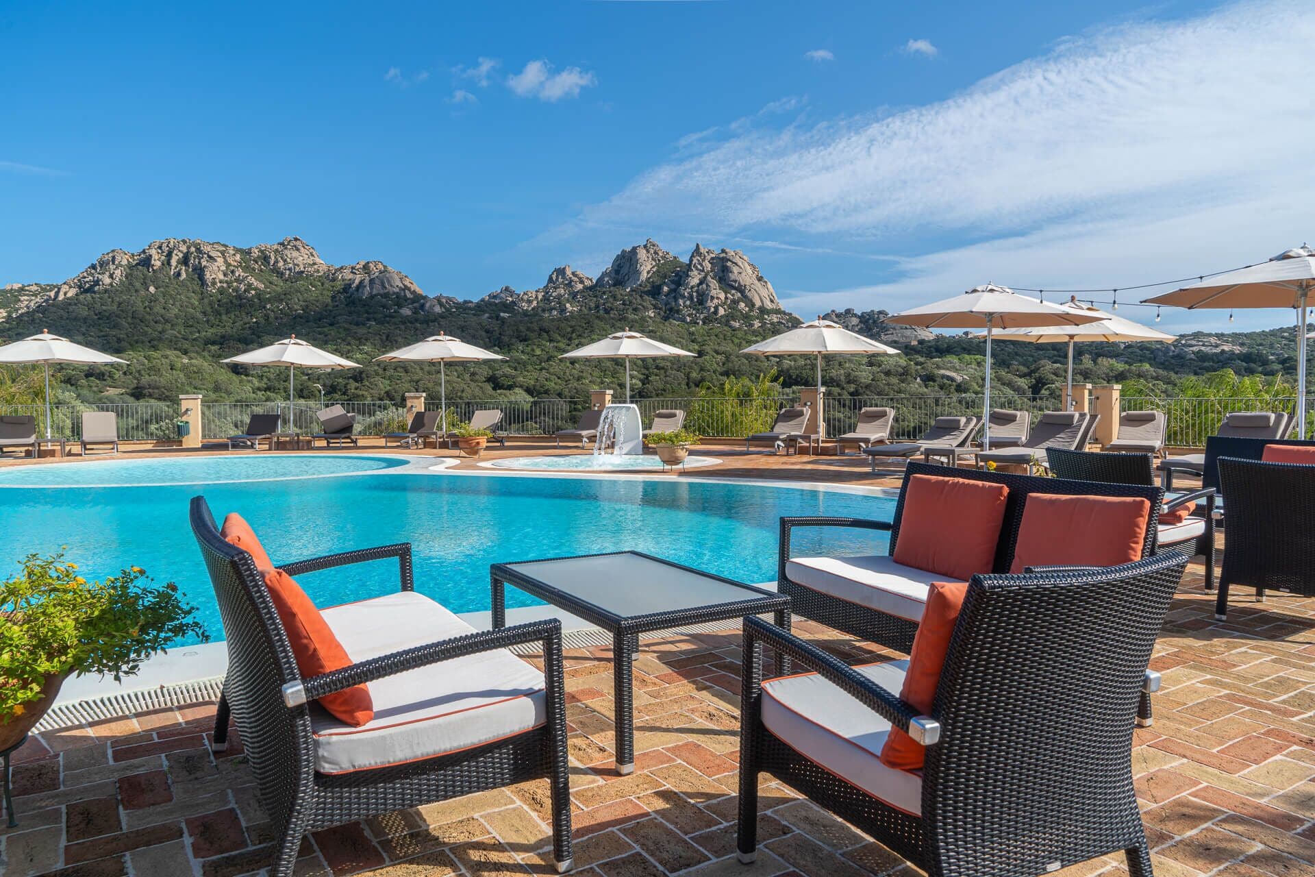 Área de piscina com espreguiçadeiras, guarda-sóis e vista para montanhas.