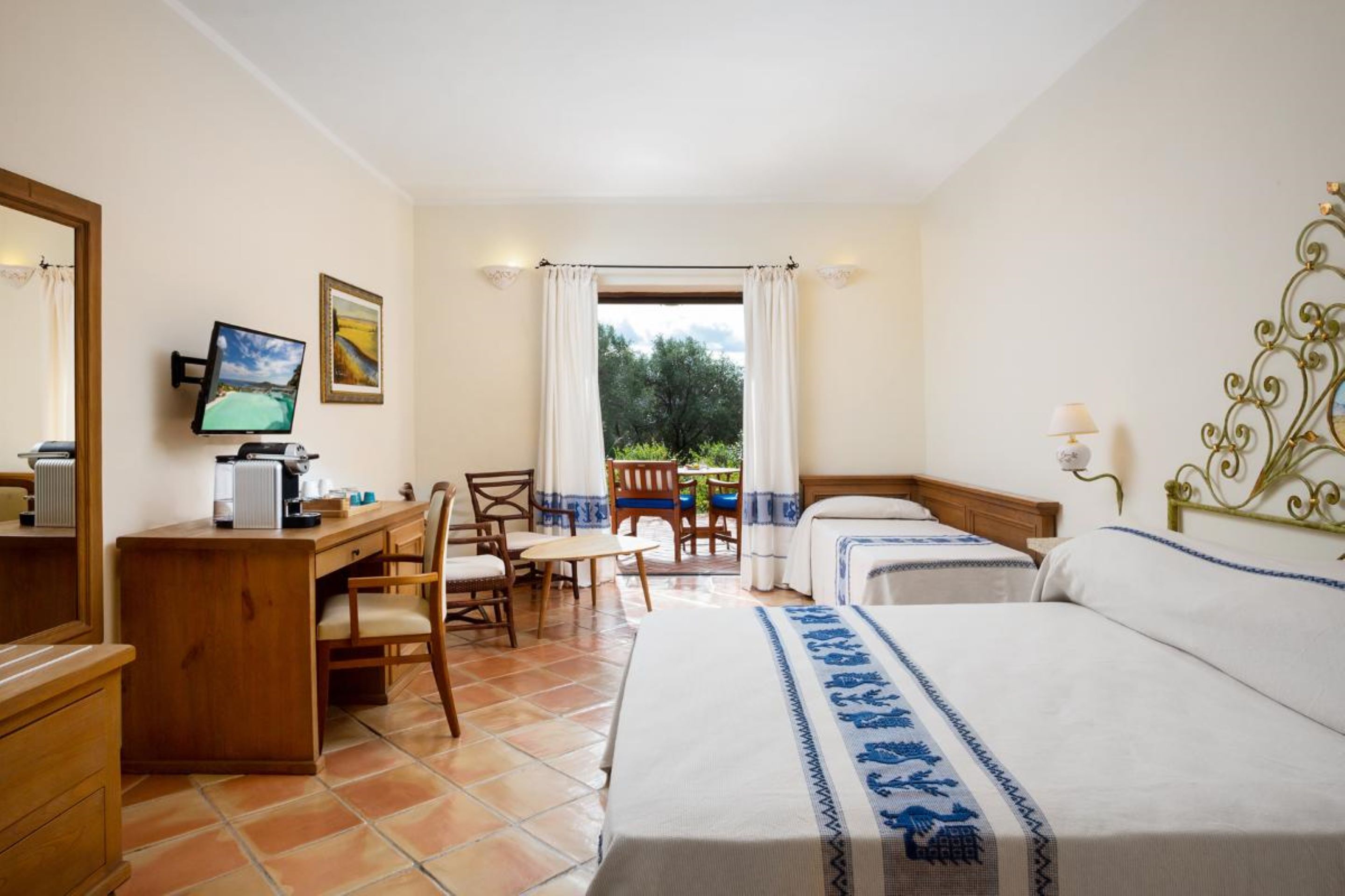 A hotel room with two beds, a desk with a computer, a chair, and a view of the outdoors.
