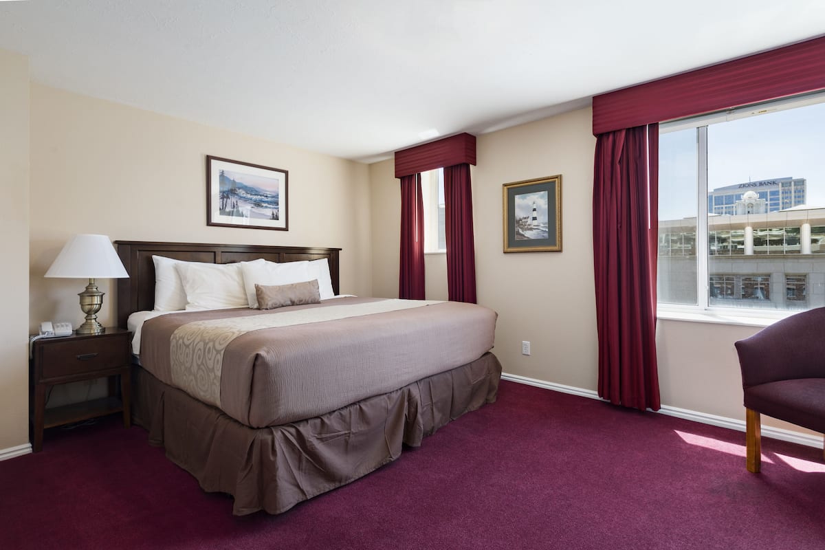 Ein Hotelzimmer mit einem großen Bett, einem Nachttisch, einer Lampe, einem Sessel und einem Fenster mit roten Vorhängen.