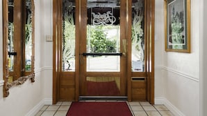 L’entrée d’un hôtel, avec un tapis rouge, une double porte en bois, un lustre et des œuvres d’art encadrées accrochées aux murs.